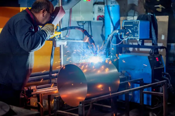 Persona equipada con traje de protección trabaja en un taller usando máquina especializada en la reparación de soldadoras para mejorar rendimiento.2.reparacion de soldadoras.jpg