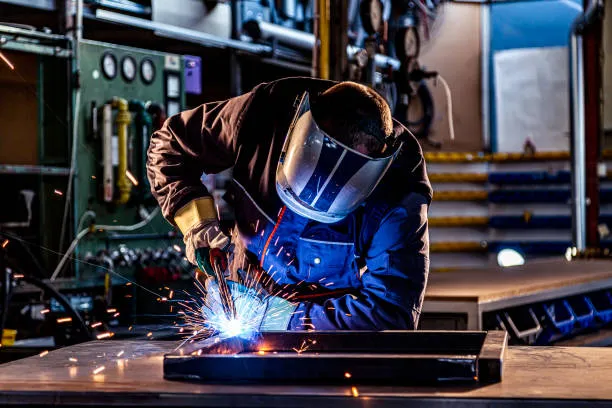 Operador con casco y guantes de seguridad manipula equipo de soldadura en taller realizando ajustes en la reparación de soldadoras. 3.reparacion de soldadoras.jpg