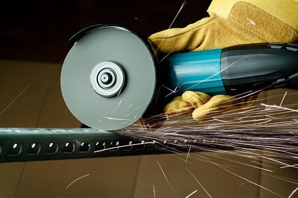 Persona operando un esmeril en funcionamiento para desbastar metal, con chispas saliendo de la superficie y mostrando el uso correcto y seguro del esmeril en un taller industrial.
