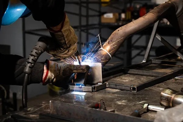 Hombre soldando mientras regula el amperaje de soldadura según el espesor del materia